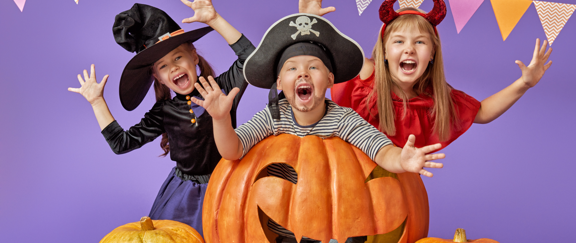 Three children in fancy dress standing behind an orange pumpkin
