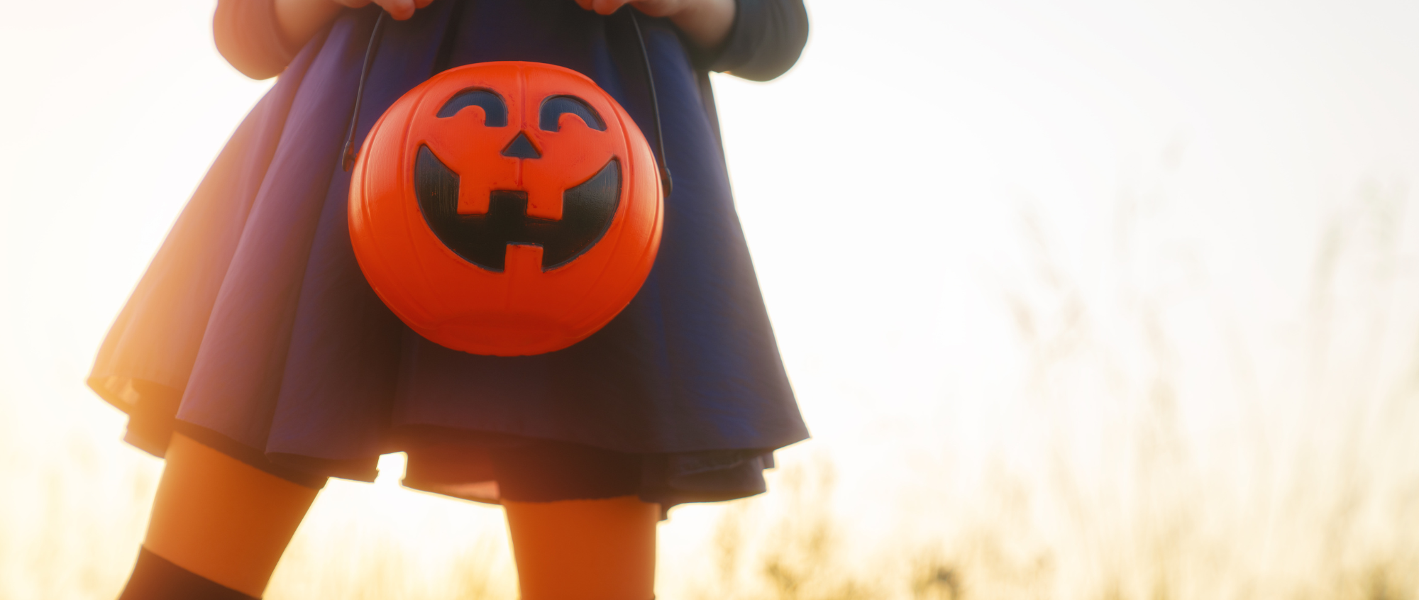 Child with black dress holding an orange pumpkin