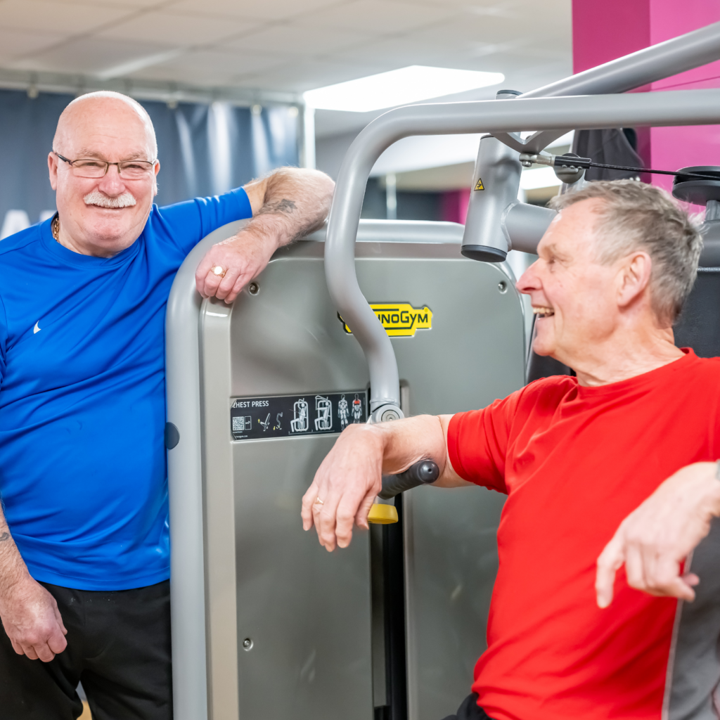 A man with a blue shirt smiling alongside a man with a red shirt smiling