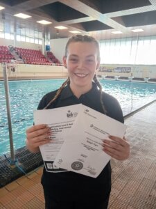 Photo of girl standing near a pool holding certificates