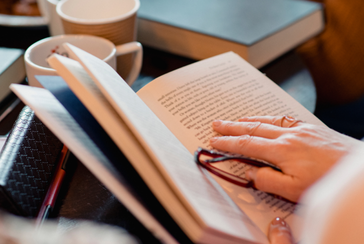 Person with book and glasses in hand