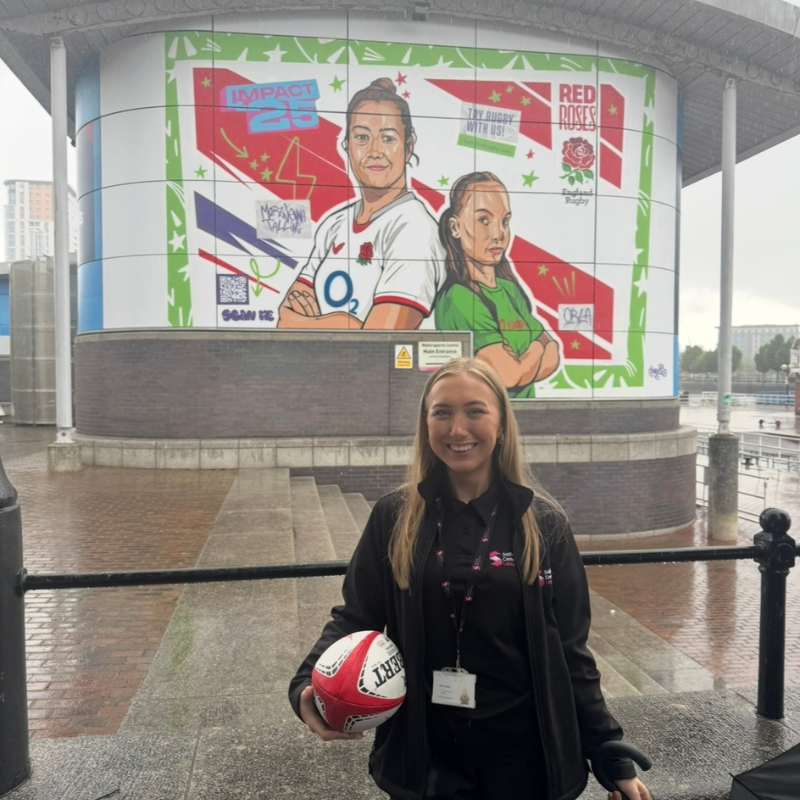 Mia standing in front of the Women's Rugby World Cup Mural in Salford