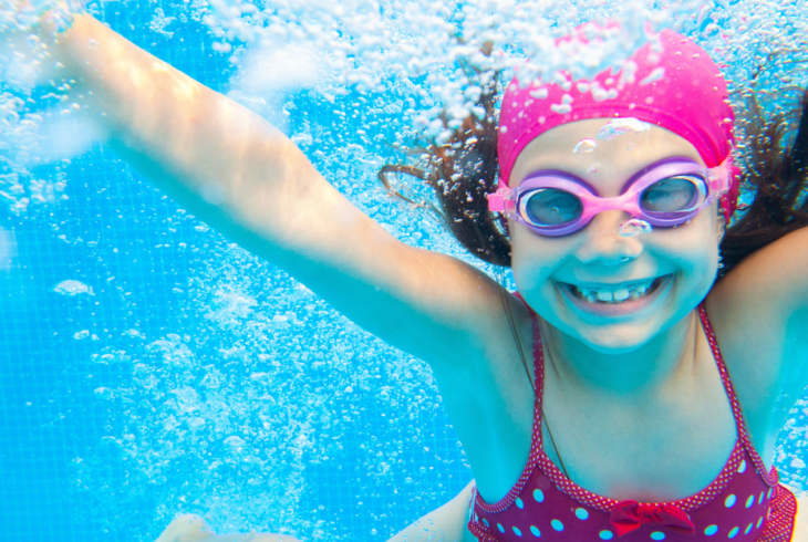 Girl swimming underwater with goggles and swimming hat