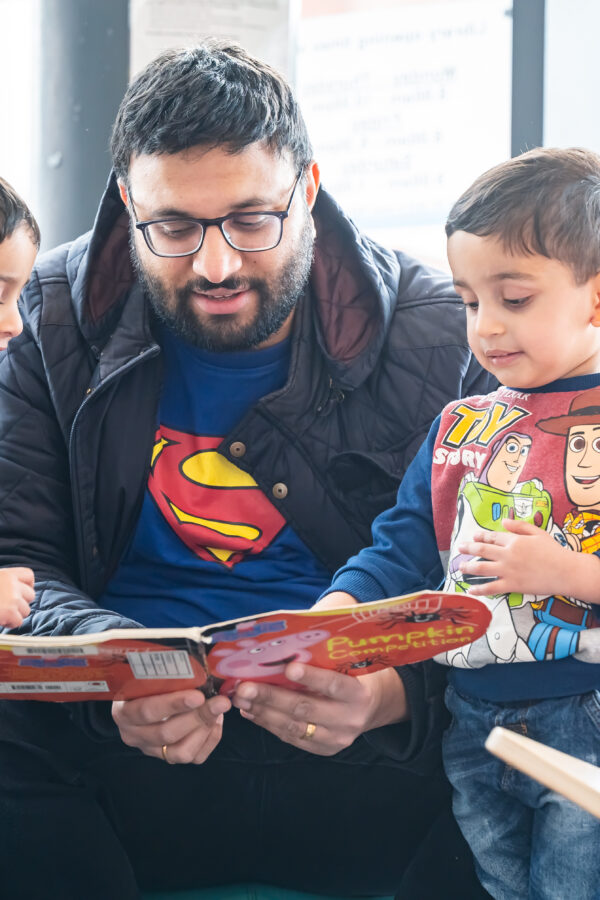 A father reading book to his 3 children int eh children's libraries who are all smiling and enjoying the story