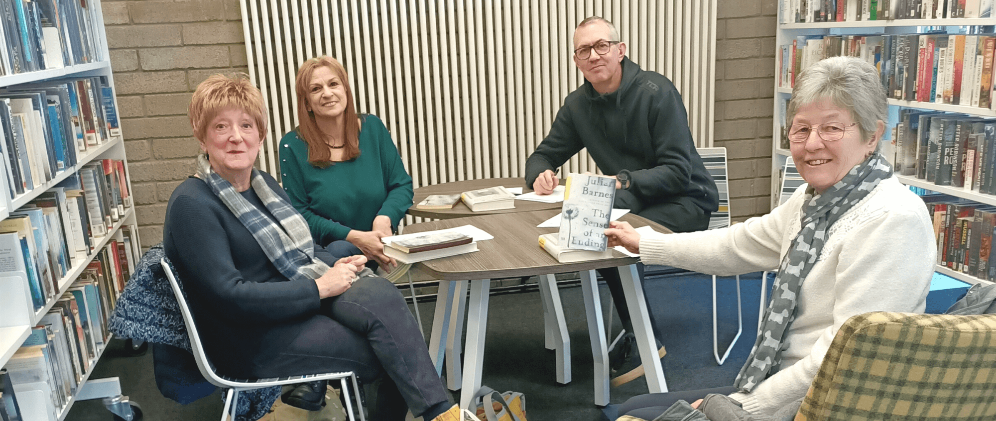 A group of adults sat around a table with a book as part of the reading groups