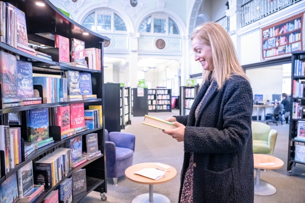 A lady is viewing a book off a shelf in the library
