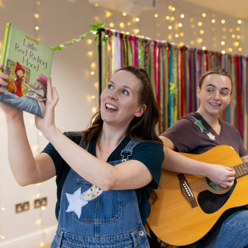 Two women, one holding a book, the other a guitar