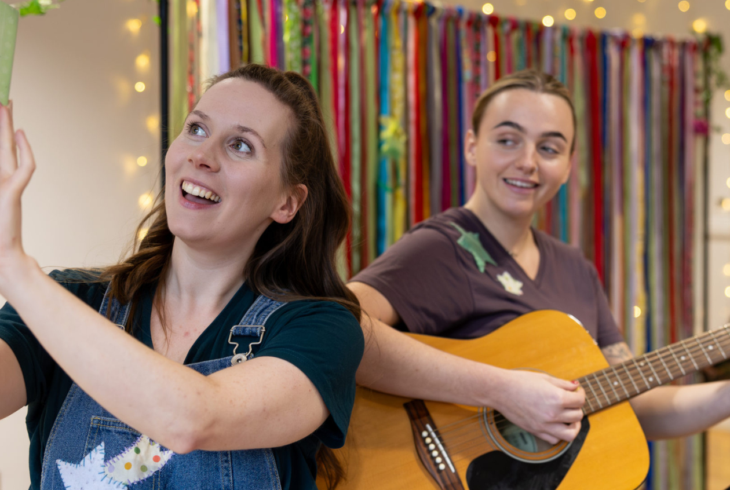 Two women, one holding a book, the other a guitar