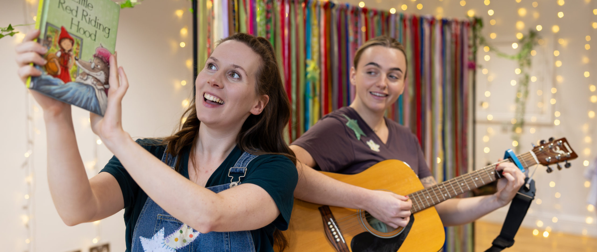 Two women, one holding a book, the other a guitar