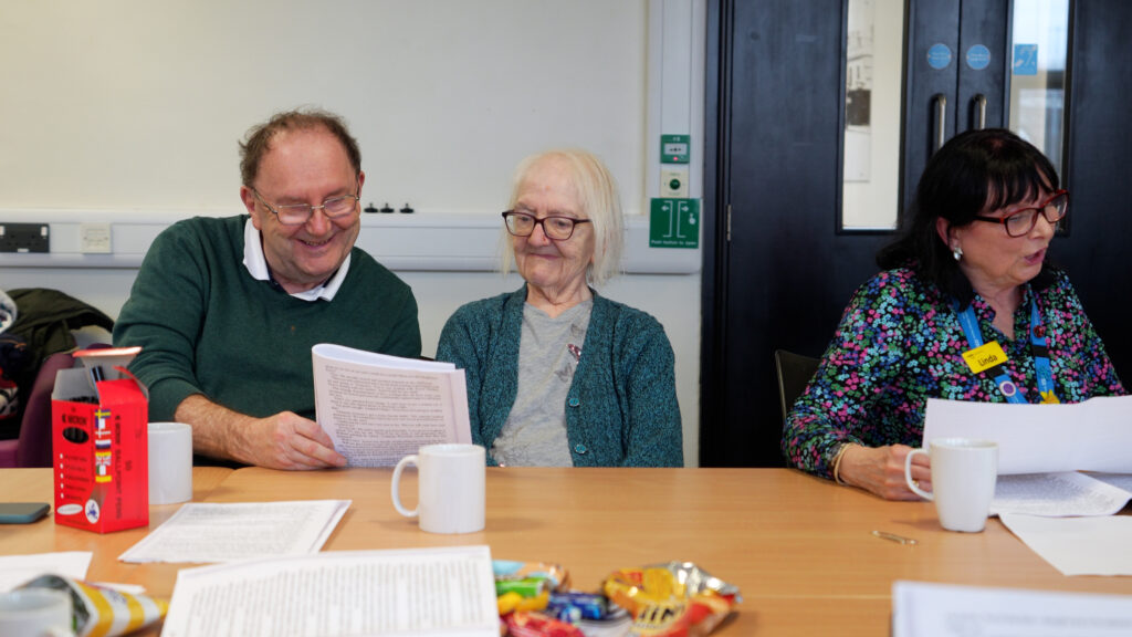 A man and older lady reading from a paper together in a Salford Library group