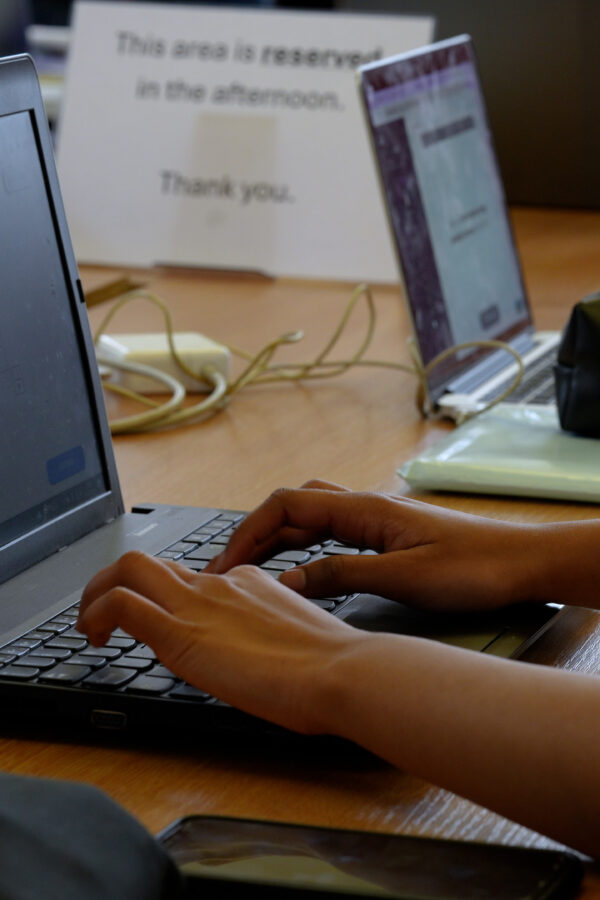 Some hands working on a laptop on a table with other laptops