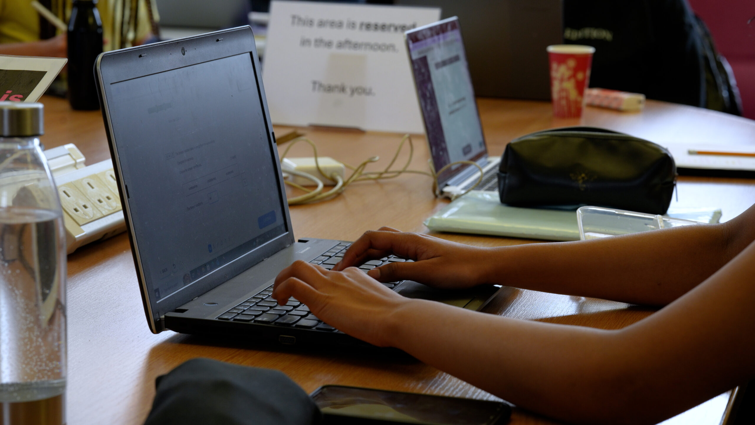 Some hands working on a laptop on a table with other laptops